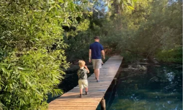 Parent and child walking along a scenic boardwalk beside the water at a Temecula Valley lakeside retreat with family-friendly outdoor recreation and nature experiences
