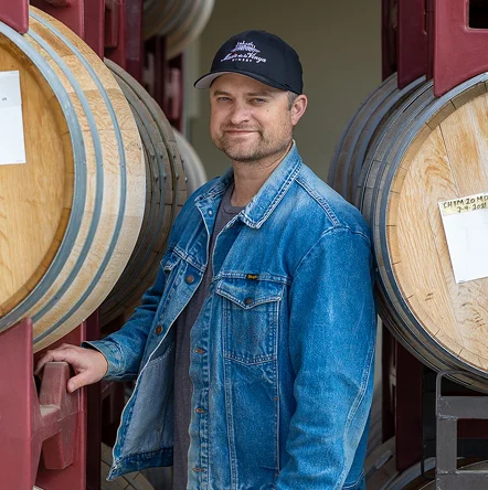 Portrait of Justin Knight, Estate Winemaker, standing beside wine barrels at a Temecula winery cellar facility