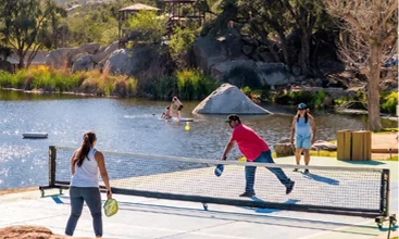 Guests enjoying pickleball and outdoor recreation beside a scenic lake at a Temecula Valley resort with family-friendly amenities and waterfront activities