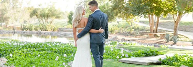Bride and groom embracing beside a scenic lakeside garden during a wedding celebration at a Temecula Valley venue with waterfront views and natural surroundings
