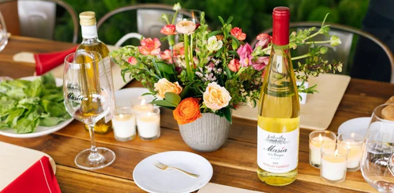 Bottle of wine, fresh floral centerpiece, and elegantly set dining table prepared for a gourmet wine and food experience in Temecula Wine Country.
